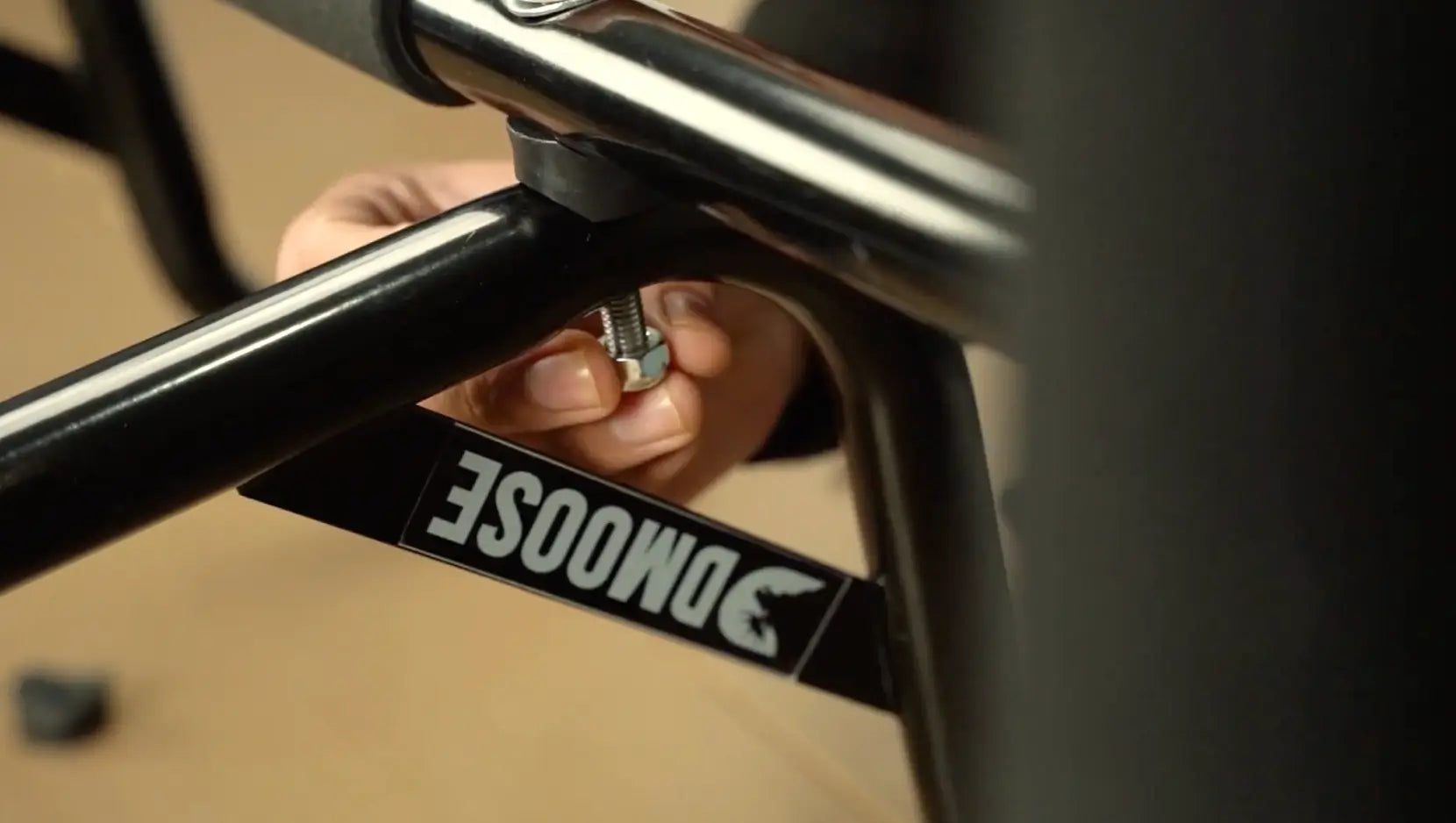 Close-up of hands hand-tightening a bolt on the black steel frame of the DMoose doorway pull-up bar