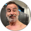 Sam E., a man in his fifties with a grey beard, smiling in a gym locker room